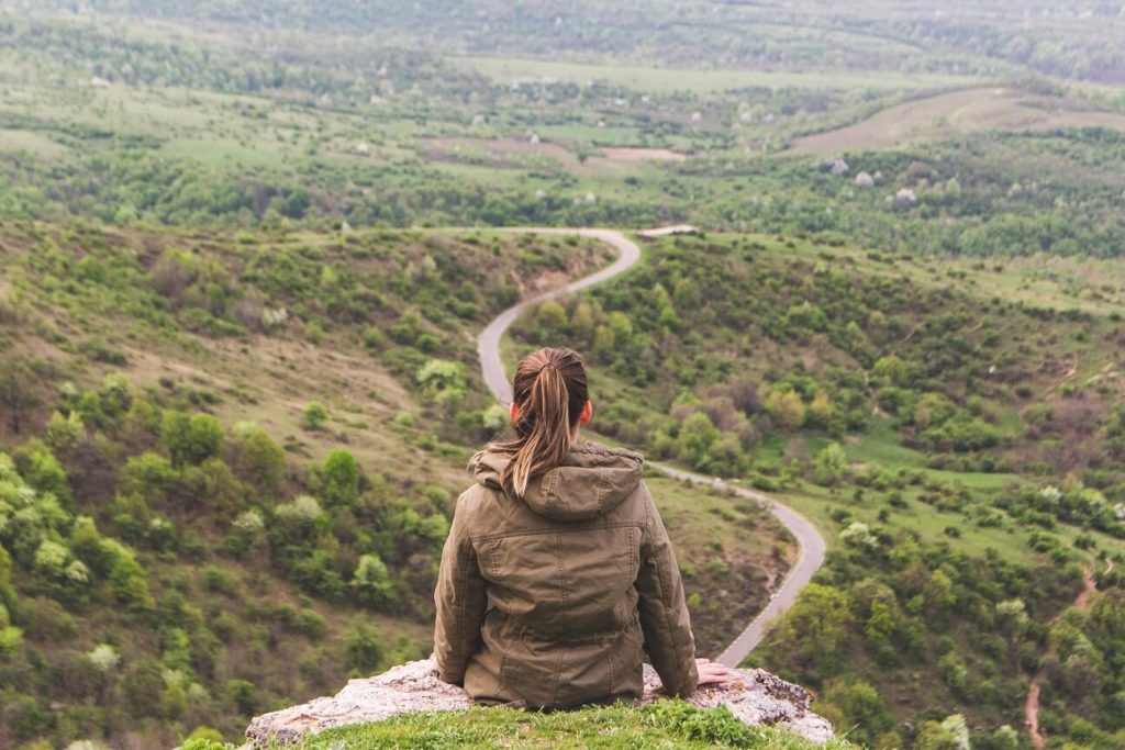 Woman sitting on mountain looking down at the winding road on a journey