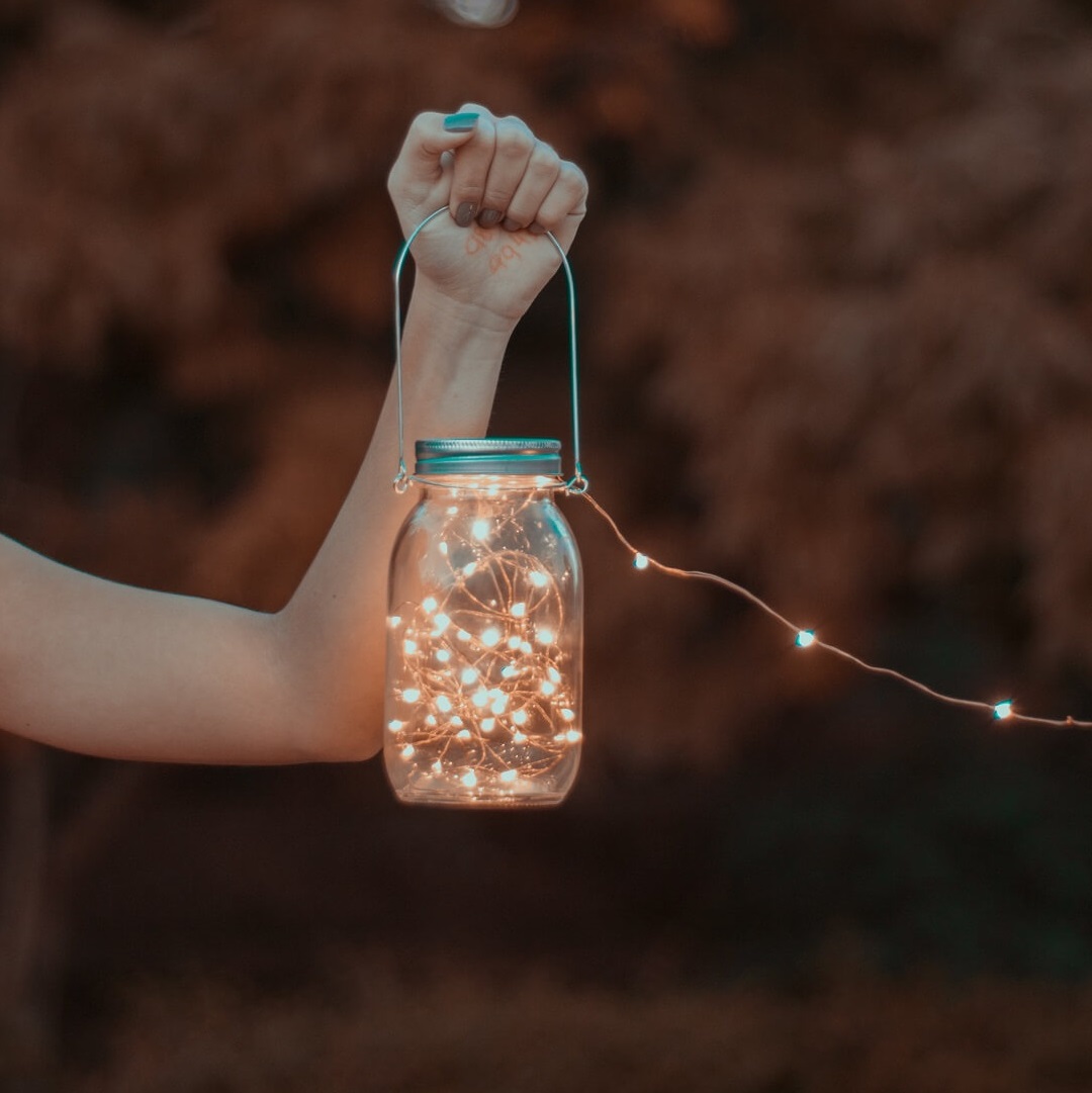 woman holding a jar of tiny lights be the light