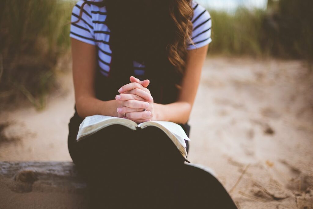 woman praying over Bible outside sandy beach