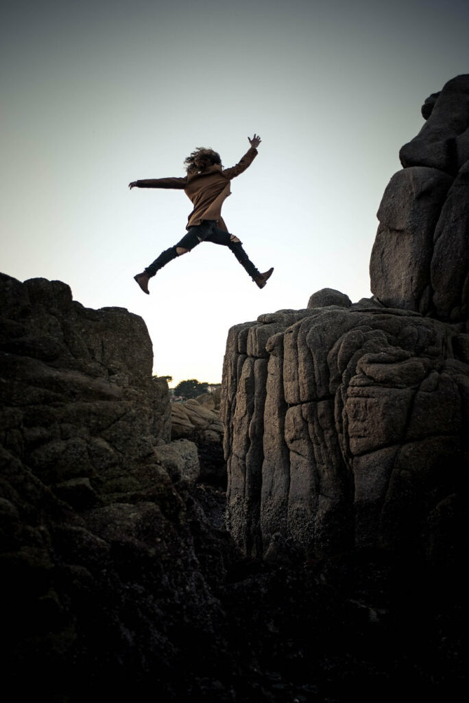 Woman jumping over a rock formation in a mountain scene.
