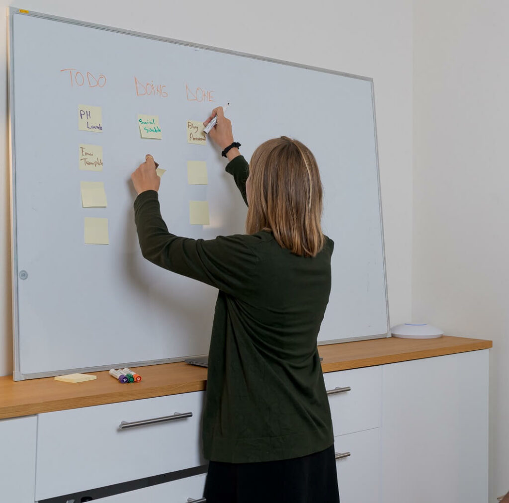 Woman learning how to prioritize your life by arranging sticky notes on a white board.