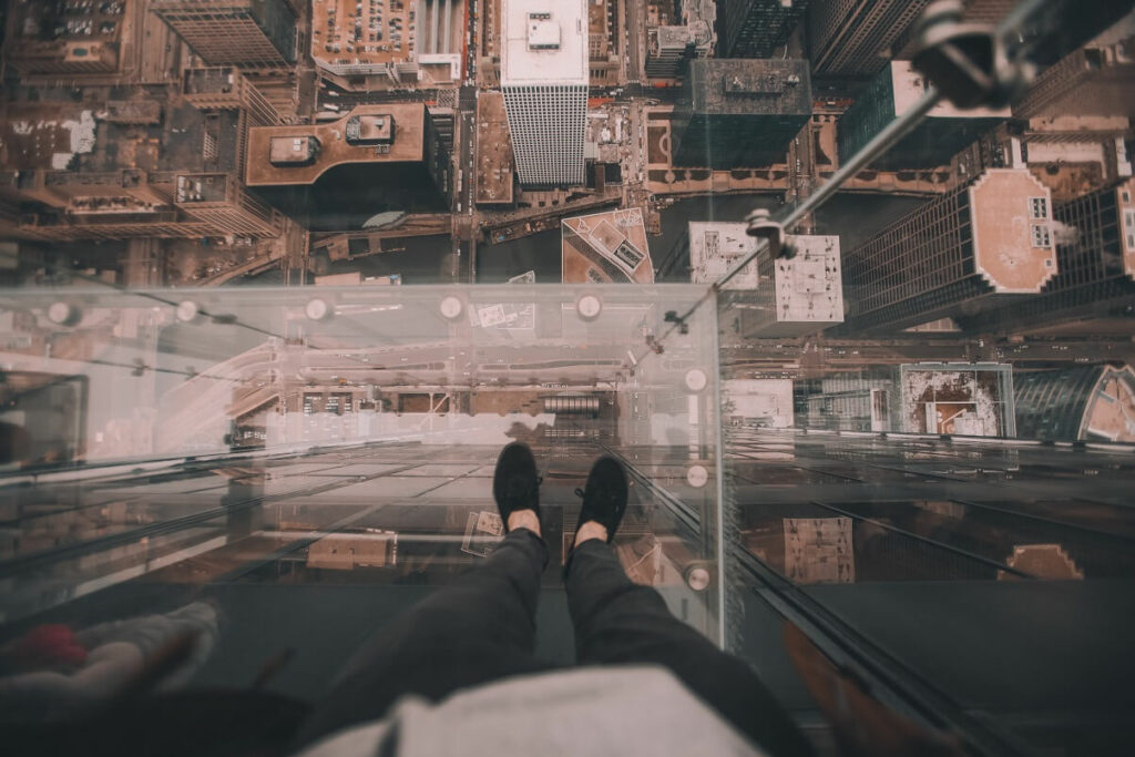 woman standing on a glass floor overlooking the edge of a high rise building for the blog post how to overcome your fears and transition into your own business.