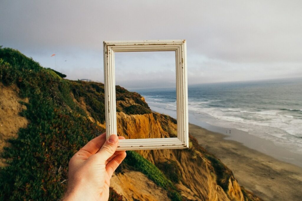 Oceanside image with person holding up a picture frame to show the reframing that is needed to go from hustle culture to God's wisdom culture