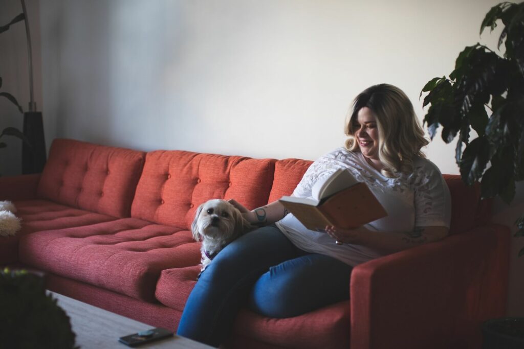 Woman reading a book while petting dog.