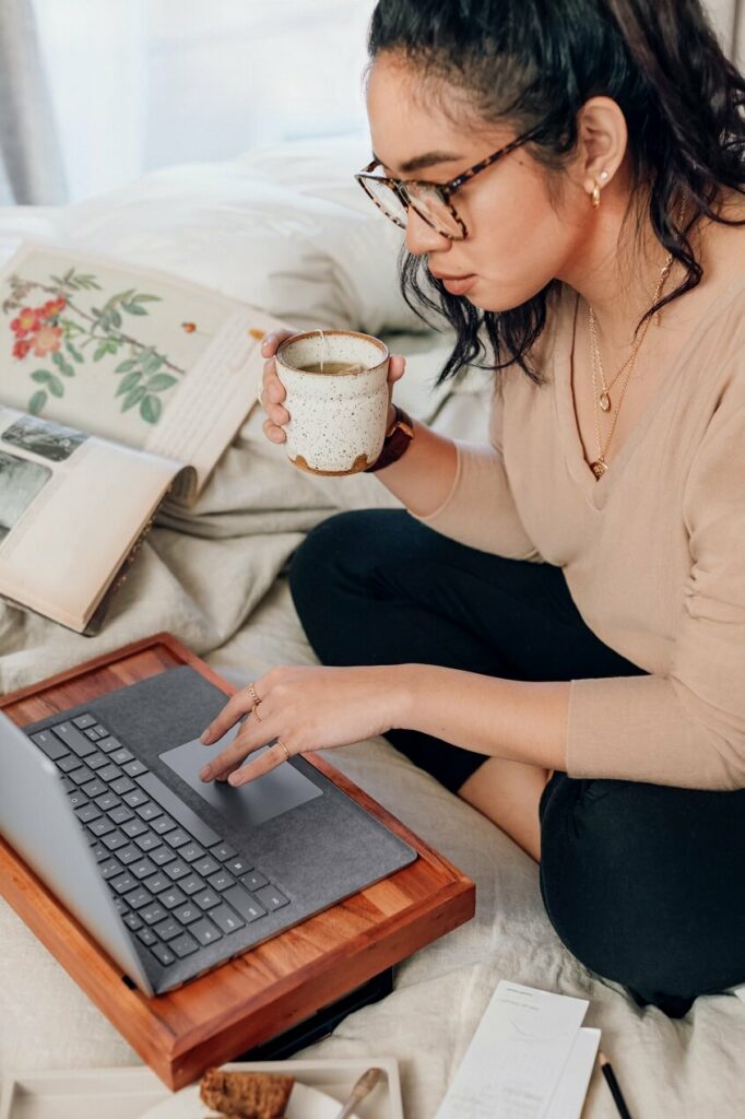 Image of a woman working at a laptop with a cup of coffee showing that simplifying is needed to learn how to be an intentional entrepreneur